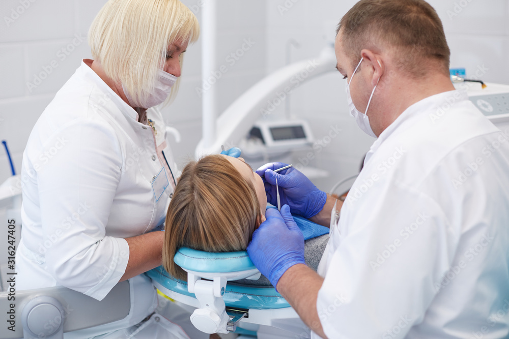 Fototapeta premium Doctor dentist treats teeth of a beautiful young girl patient. The girl on reception at the dentist. Doctor dentist treats tooth