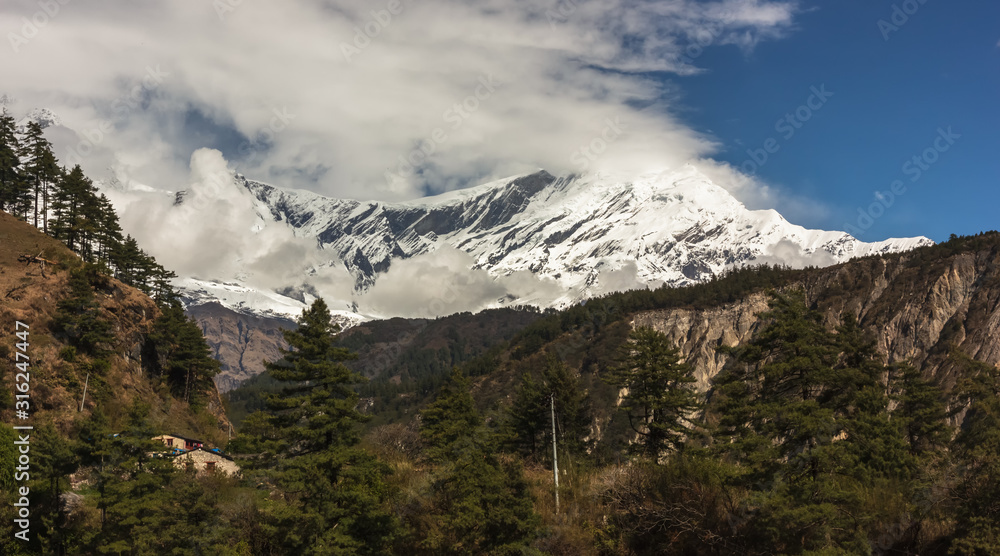Clouds cover the snow covered rock faces and peak of Tukuche mountain in the village of Kalopani on the Annapurna Circuit trail in the Nepal Himalaya.