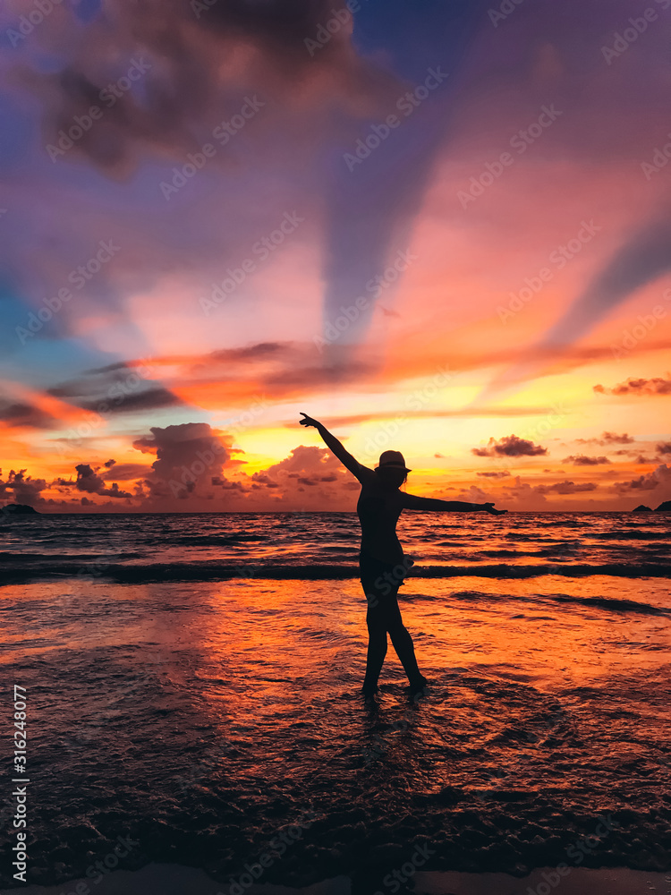 Silhouette of a thin girl in a hat on the seacoast on the background of  wonderful sunset. The sun's rays break through the clouds. Sense of freedom. Mesmerizing landscape. The vertical position 
