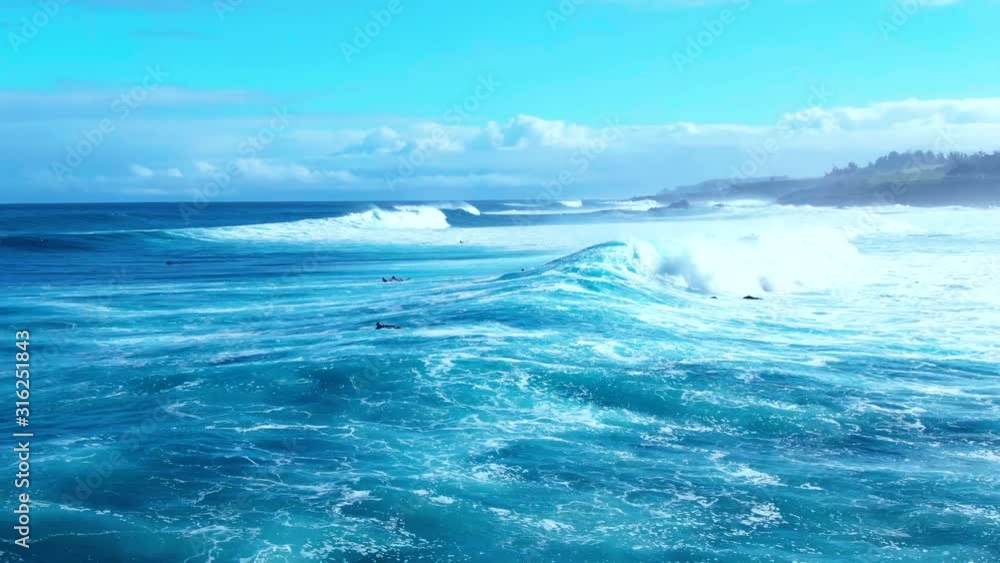 Surfers swim towards big waves coming from deep blue ocean, splashing and foaming over calm turquoise lagoon of tropical island in Hawaii