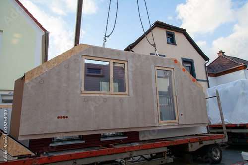Wallpaper Mural The component for the prefabricated house hovers on the crane rope above the truck trailer. Three houses and the crane boom can be seen in the background Torontodigital.ca