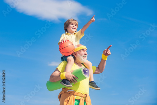 Happy grandfather giving grandson piggyback ride on his shoulders pointing and looking up. Different generations.