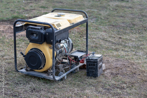 close-up. Street lighting. A gasoline-powered generator that produces current. A car battery is connected for charging. Backup or emergency power source. The generator is not new photo
