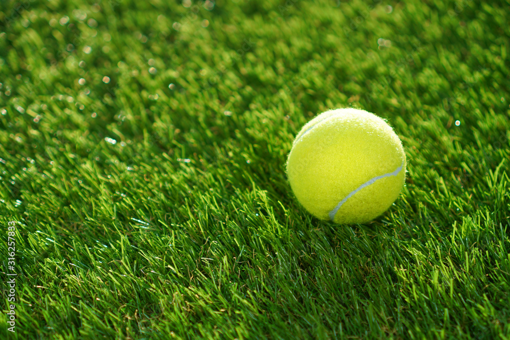 Artificial grass background. Tennis ball lying on the green soft artificial turf.