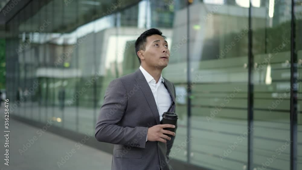 Real time portrait shot of a young Asian businessman walking back and forth with coffee in his hands. Real time portrait shot of a young Asian businessman walking back and forth with coffee in his hands.