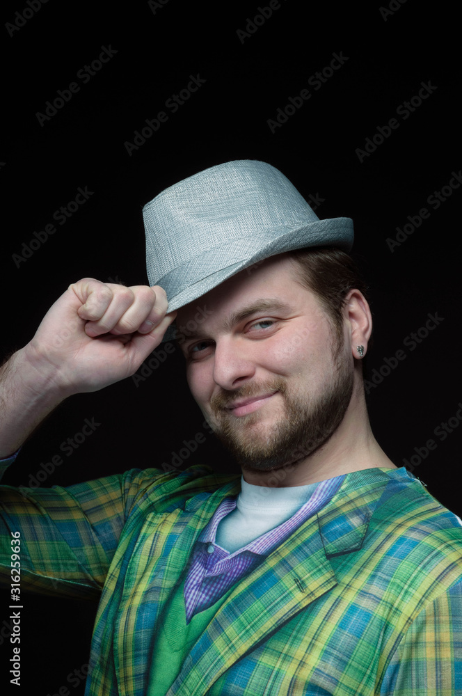 low-key portrait of handsome bearded smiling man in green checkered blazer putting on stylish grey hat isolated on black low-key portrait of handsome bearded smiling man in green checkered blazer putting on stylish grey hat isolated on black