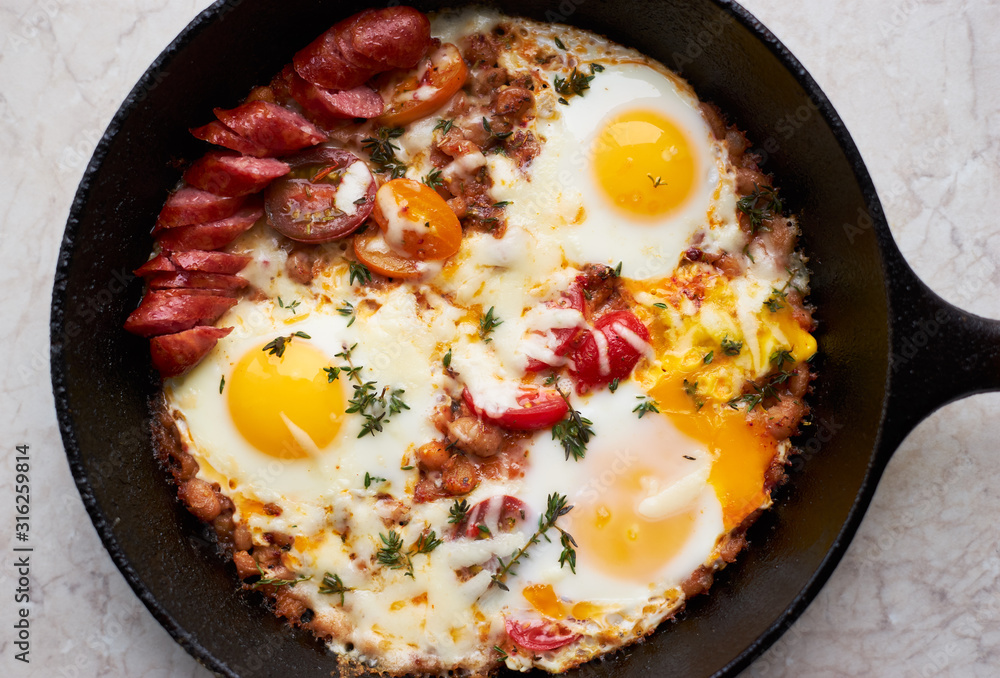 Homemade fried eggs with sausage, cheese, spices and vegetables in a pan Homemade fried eggs with sausage, cheese, spices and vegetables in a pan