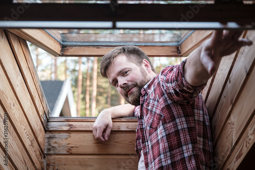 Foto Handsome bearded man stands near an open skylight in the attic.