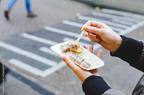 Holland herring fish in female hand outside. Traditional Dutch street food, herring fish. Stock photo street food, herring fish with onions and pickles.