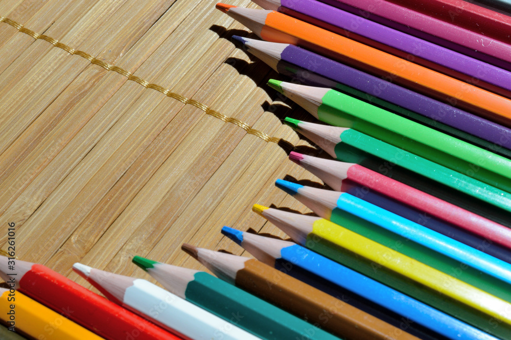 Fototapeta premium multicolored pencils laid out by an arc on a straw background.