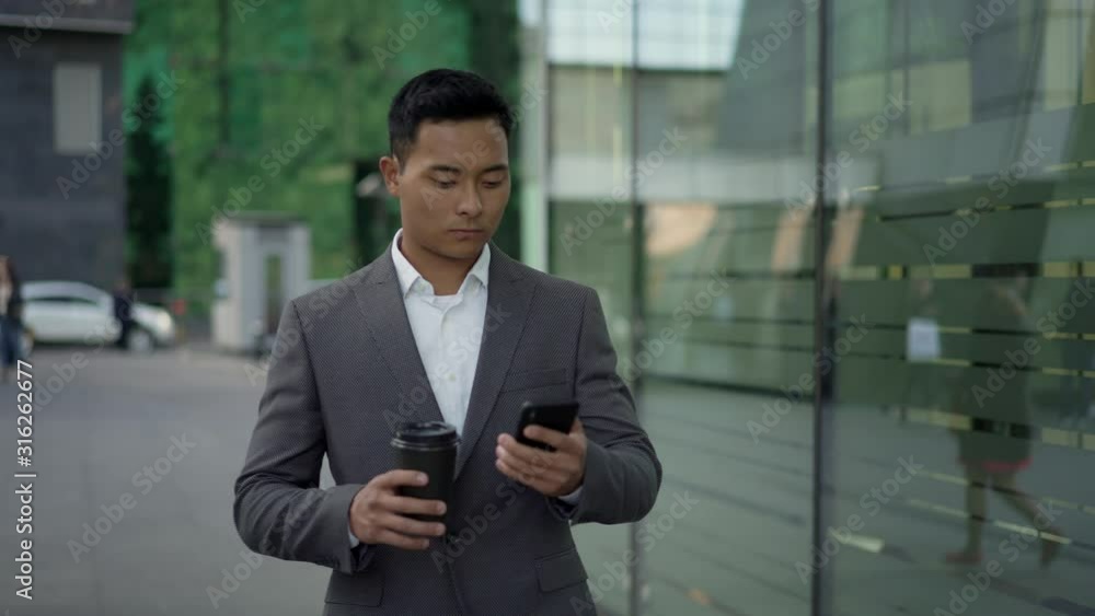 Real time portrait shot of a young businessman walking, conducting correspondence on the phone with coffee in his hands. Real time portrait shot of a young businessman walking, conducting correspondence on the phone with coffee in his hands.