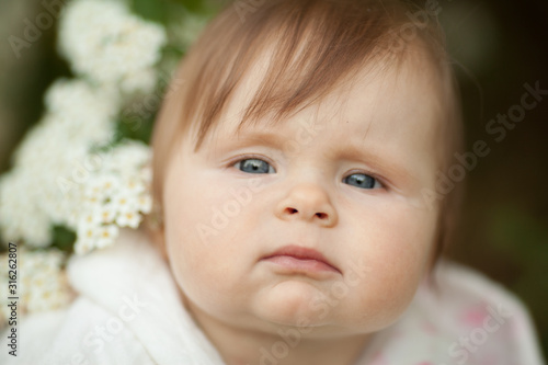 Cute little baby girl in spring in a blooming garden  looking at the camera. Beautiful portrait. Concept  spring  family. The care for the baby.