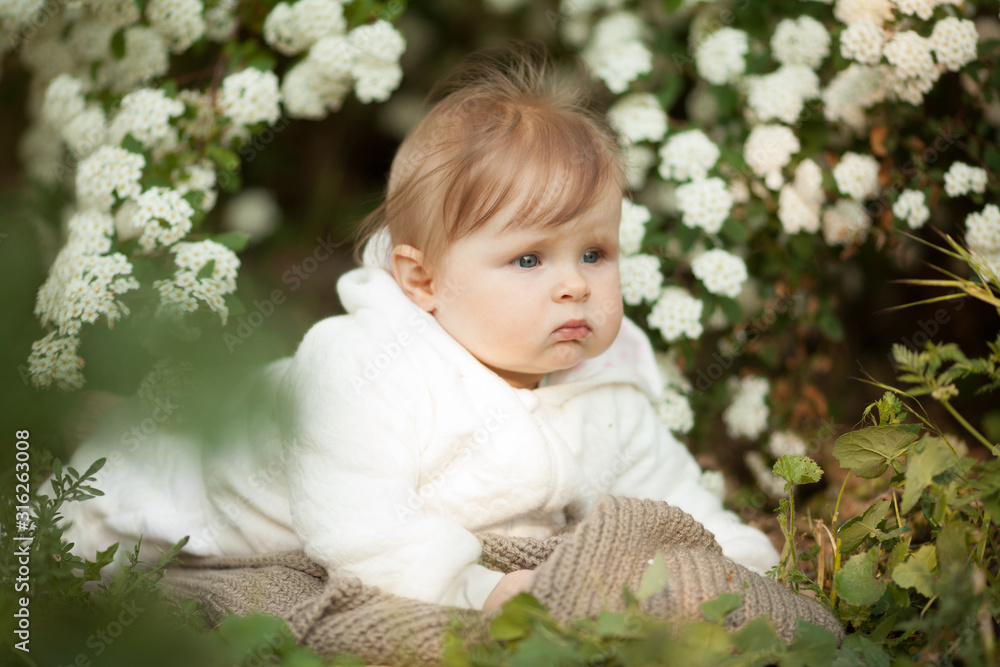 Beautiful little baby girl in spring in a blooming garden, looking at the camera. Beautiful portrait. Concept: spring, family. The care for the baby.