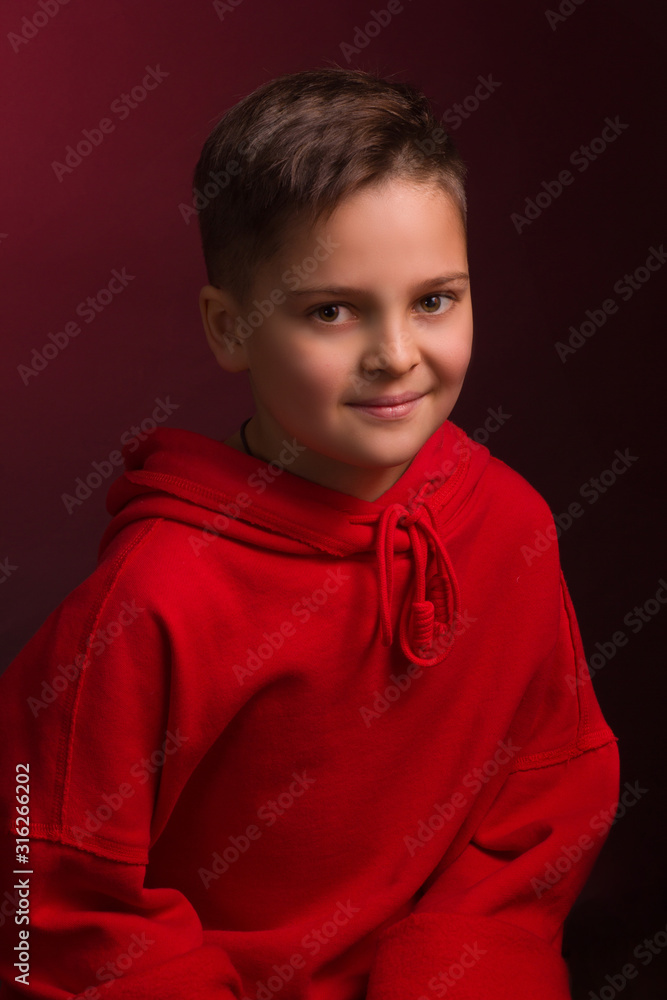 Studio portrait of a dark-haired boy, on a maroon background, in a red hoodie jacket Studio portrait of a dark-haired boy, on a maroon background, in a red hoodie jacket