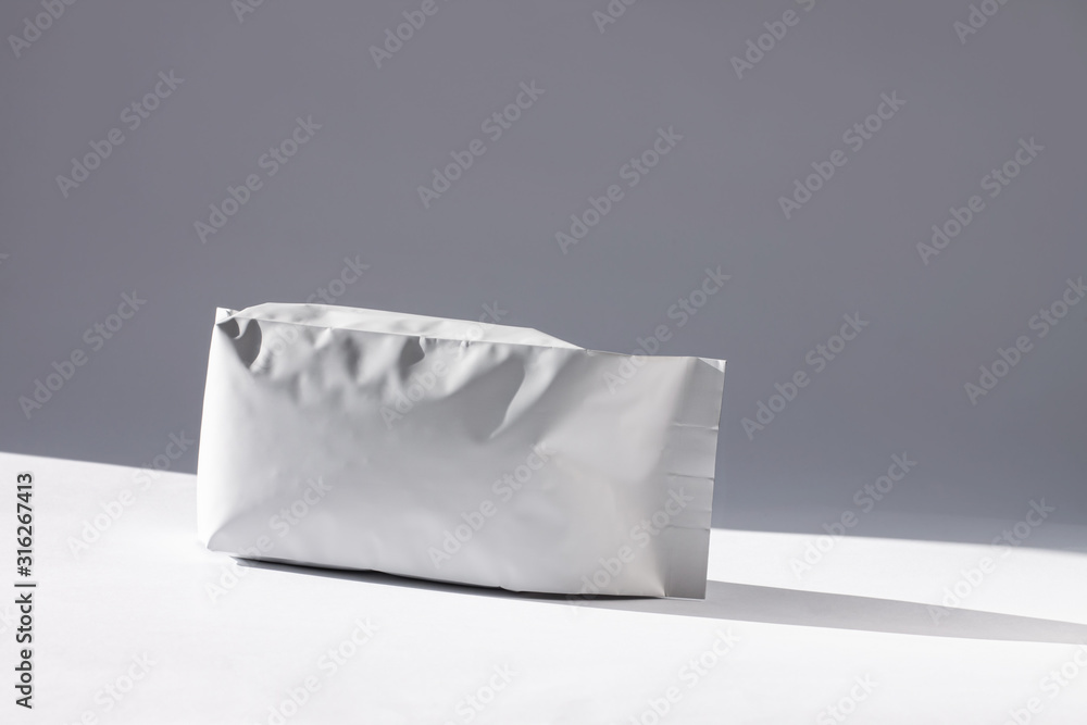 Blank foil food or drink bag on white background in minimal style, natural light shadow. Monochrome photo front view.Packaging valve and seal template mockup. Metallic coffee tea retail package design Blank foil food or drink bag on white background in minimal style, natural light shadow. Monochrome photo front view.Packaging valve and seal template mockup. Metallic coffee tea retail package design