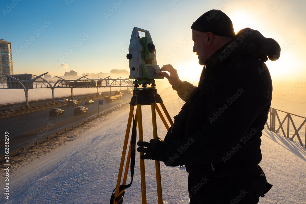 Work surveyor. Man works with theodolite. Theodolite on a tripod. Man and the instrument on the background of the setting sun. Carrying out measurements. Road works. Construction.