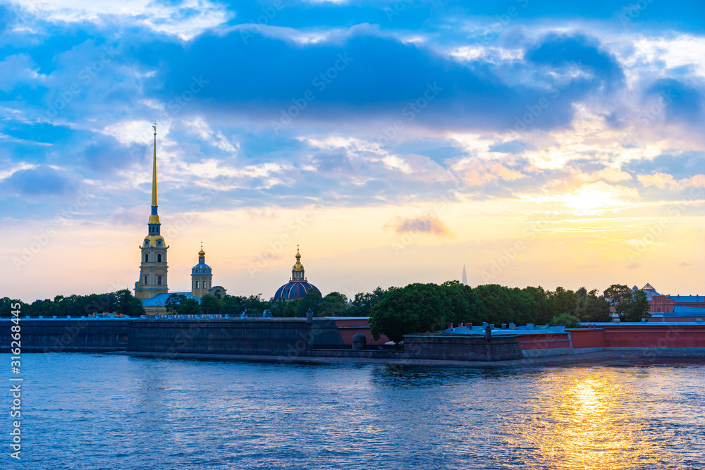 Fototapeta premium Evening Petersburg. Rivers Of St. Petersburg. Summer trip to Russia. The sun is reflected in the Neva. Peter and Paul fortress on the background of water and sky. Clouds over St. Petersburg.