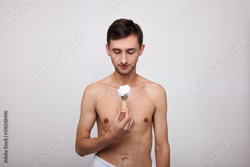 Obraz na plátně A well-groomed handsome young man holds a shaving anoint in his hand