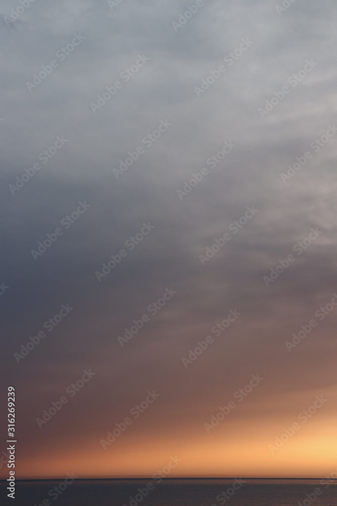 Sun behind clouds above sea skyline. Beautiful orange sky over horizon at sunset. Lonely peaceful feeling.