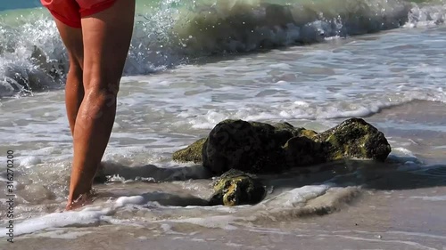 Waves wash over a rocky Florida beach while a woman casually walks in shallow surf.