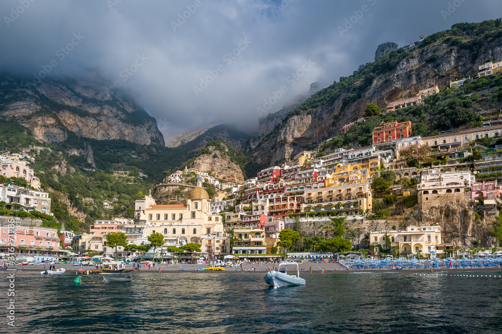 Positano bay with beach, old town on the hill. Mountain range at the background. Amalfi coast, Italy.