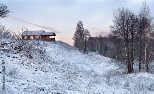 One small village house stands on a hill near a forest in the snowy winter. Concept of privacy in nature. Vacation in the country. Fresh air