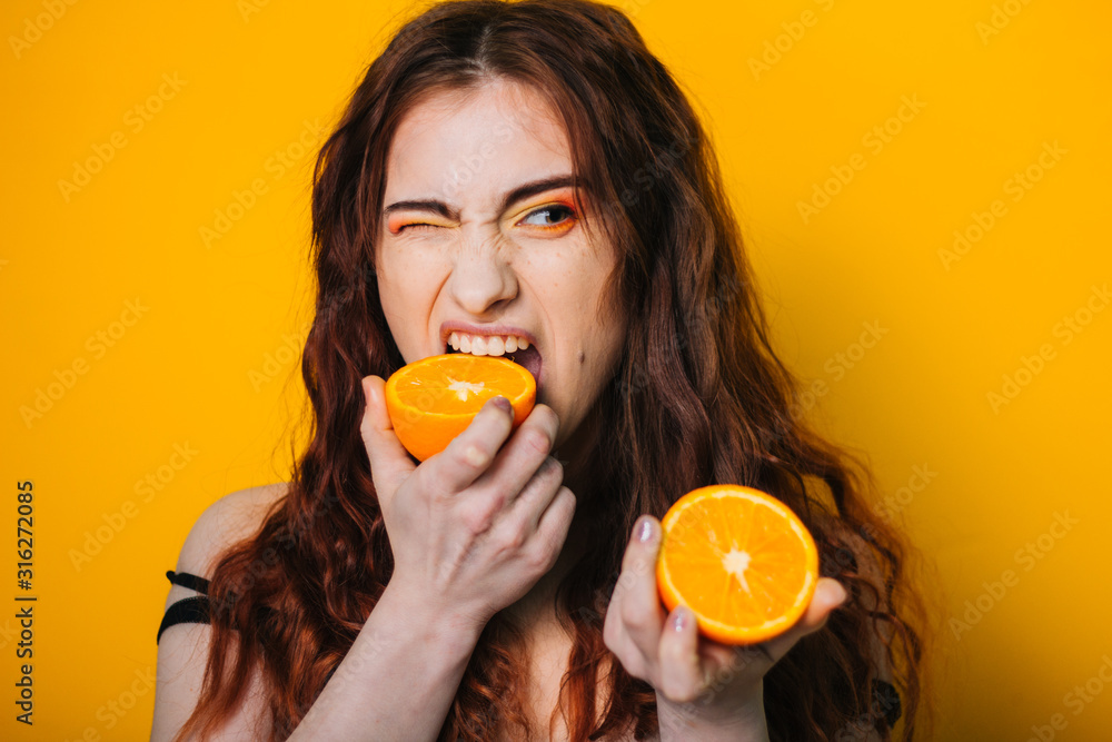 Beautiful girl on a bright yellow background. Model with fruit in hand. Two orange slices. emotion. Crooked faces Beautiful girl on a bright yellow background. Model with fruit in hand. Two orange slices. emotion. Crooked faces