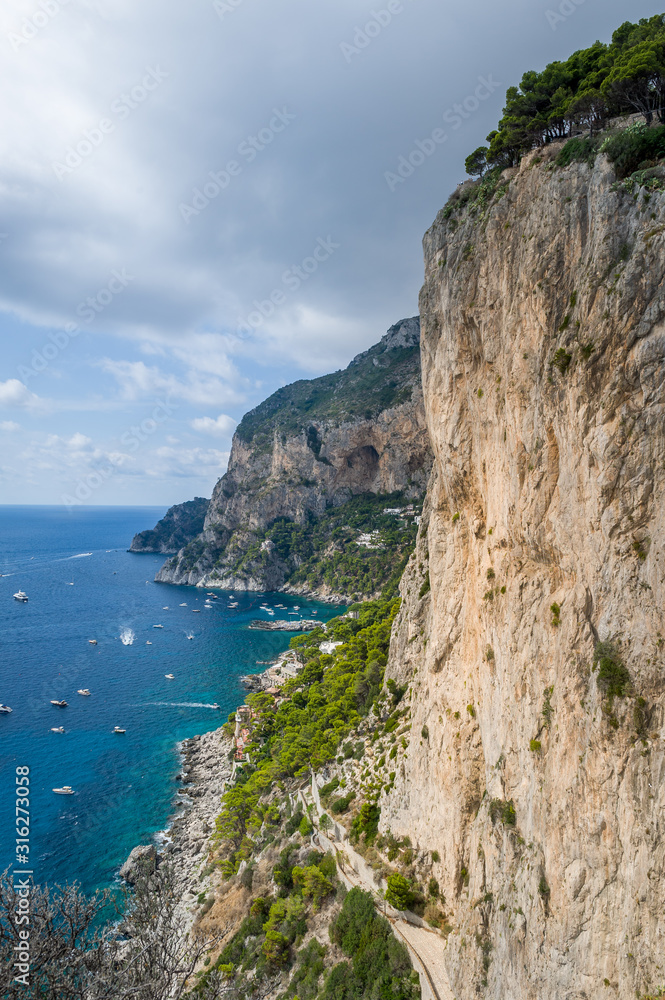 Vertical photo of rocks and cliffs of Capri island. Viewpoint to the sea bay with small local's boats and perfect climbing walls. Capri, Italy.