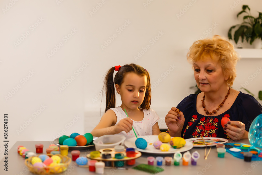Naklejka premium Grandmother with granddaughter are coloring eggs for Easter.
