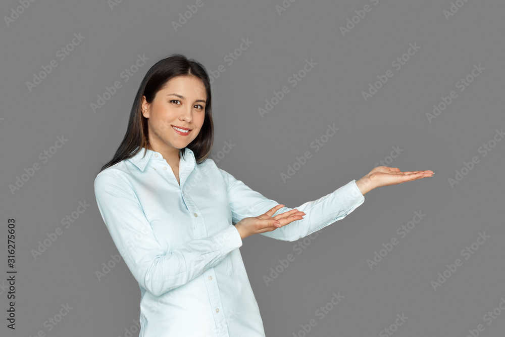 Space for Text or Product. Young woman standing isolated on grey showing aside smiling cheerful to camera Space for Text or Product. Young woman standing isolated on grey showing aside smiling cheerful to camera