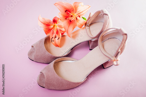 Female pink shoes with lily flowers on pink background. Stylish suede footwear. Women fashion