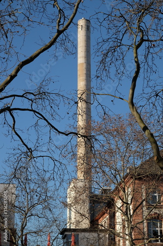 Schornstein eines Kraftwerk vor blauem Himmel im Sonnenschein im Winter hinter kargen Ästen am Senckenberg Museum im Stadtteil Bockenheim am Westend von Frankfurt am Main in Hessen photo