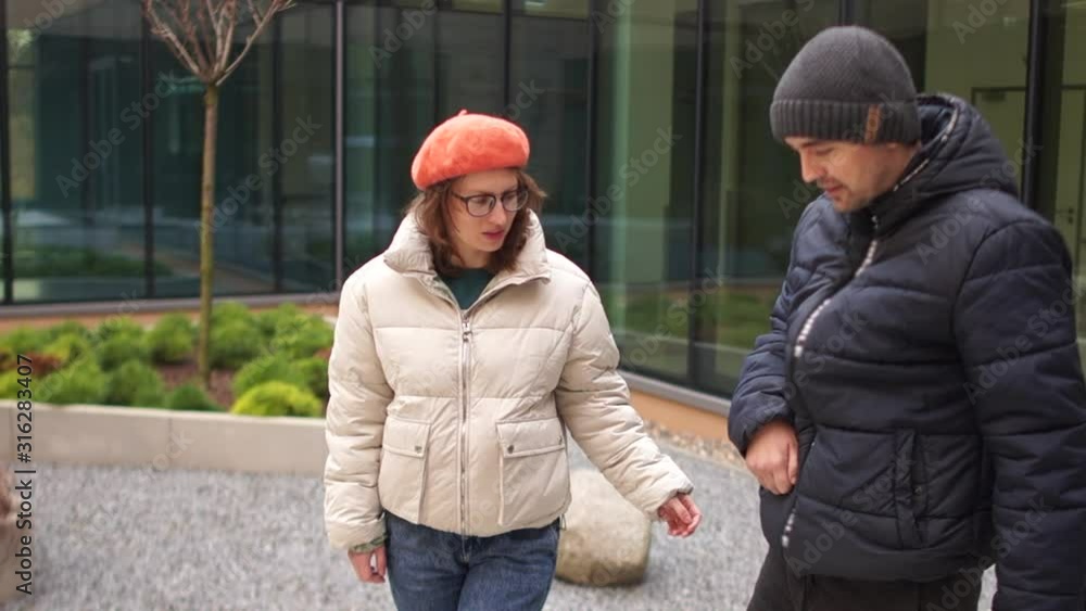 Young man in a black jacket and hat learns to walk again after a stroke or accident. Paralysis of extremities. Nearby is his girlfriend, a woman in a white jacket Young man in a black jacket and hat learns to walk again after a stroke or accident. Paralysis of extremities. Nearby is his girlfriend, a woman in a white jacket