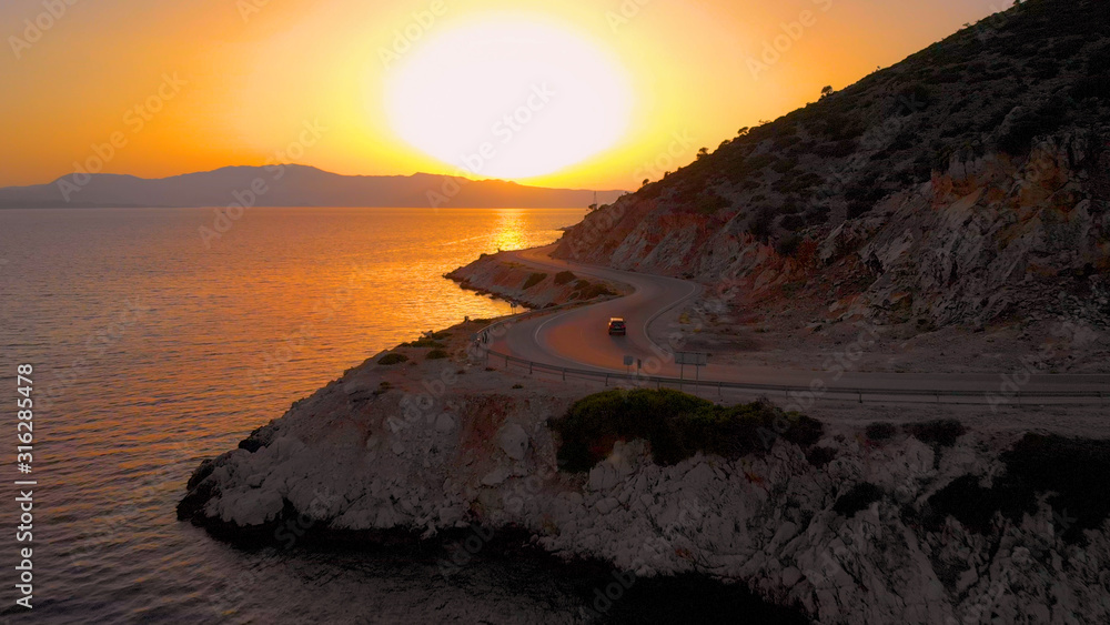 DRONE: Car drives down the asphalt road leading along the beautiful shoreline.