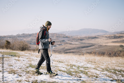 Hiker man holding poles and climbing mountain with snow