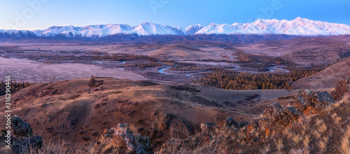 Panorama of snow peaks at dawn view from the hill to the river valley below.
