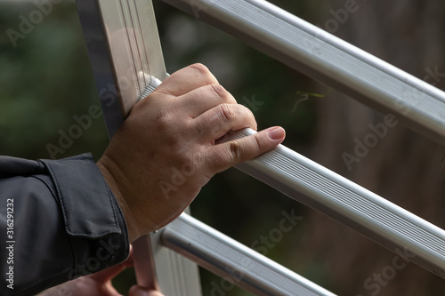 mans hand on a silver ladder ready to climb up on a home