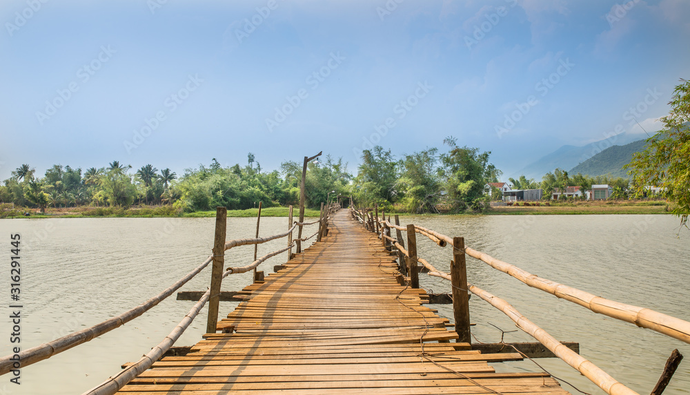 First-person view of a wooden and not safe railing bridge over the river in Vietnam.