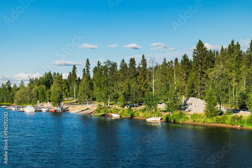 Panoramic summer view of Iijoki river near Municipality of Ii in the region of Northern Ostrobothnia, Finland. The old wooden pier and boat on the shore © sonatalitravel