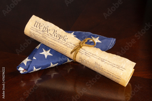 The U S Constitution rolled tied with cord displaying We The People on a U S Flag on an oak table with reflection