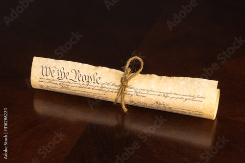 The U S Constitution rolled  tied with cord displaying We The People on an oak table with reflection