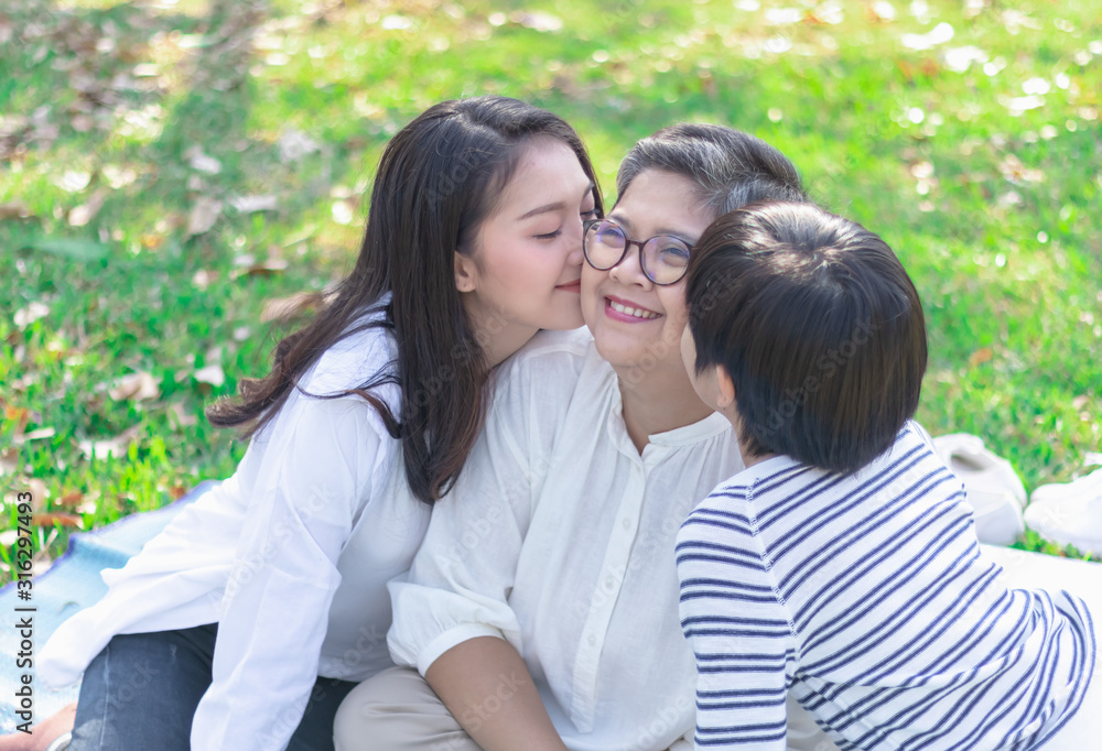 Fototapeta premium Asian lovely young daughter and grandson kiss happy and healthly senior woman or pleasure grandmother in moment of beautiful love in the park. Family generation relationship or bonding photo concept