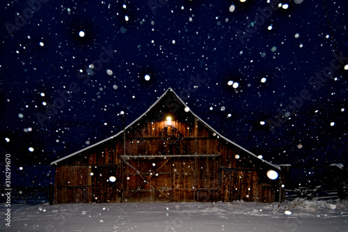 A peaceful snow scene with Old Rustic Barn with peak light and falling snow at night, Eastern Oregon 