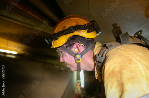 Closeup construction worker wearing safety helmet, clear glass ears noise protection headlamp while performing working inside confined spaces photo