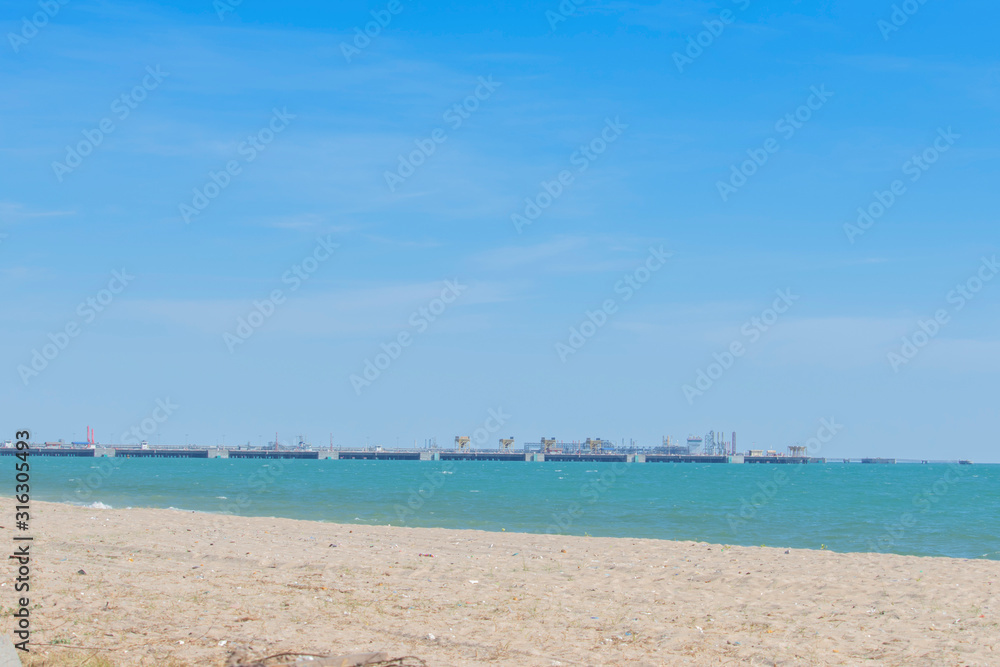 Deep water port for loading goods in the sea and clear sky. The beach has a small piece of plastic waste in the sand.