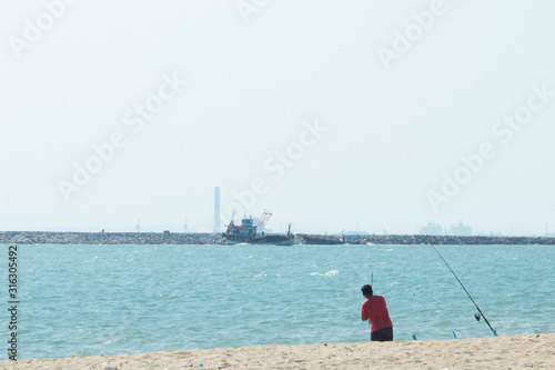 Men wearing red shirts were fishing with a hook. On the beach front, a fishing boat was returning to shore and people wearing fishing.