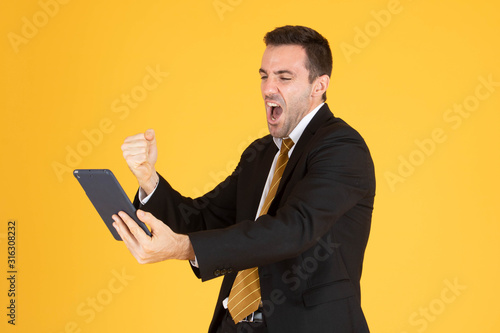 Portrait of cheerful businessman using tablet on yellow background.