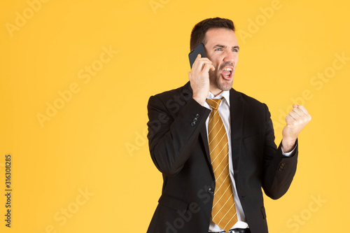 Portrait of happy businessman using smartphone on yellow background.