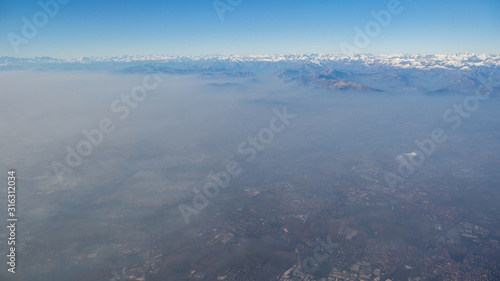 Aerial view of the smog and fog that covers the Po Valley in Italy. Landscape from airplane window. Pollution due to low rain and no wind. In the background the Alps