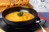 Cream carrot tomato orange soup with thyme garnish in black bowl with sliced bread